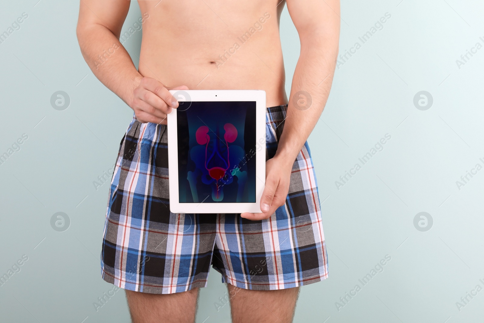 Photo of Young man holding tablet with urinary system on screen against color background