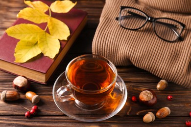 Cup of aromatic tea, book and soft sweater on wooden table indoors, above view. Autumn atmosphere