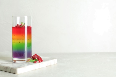 Photo of Board with glass of colorful jelly, spoon and pomegranate seeds on light table. Space for text