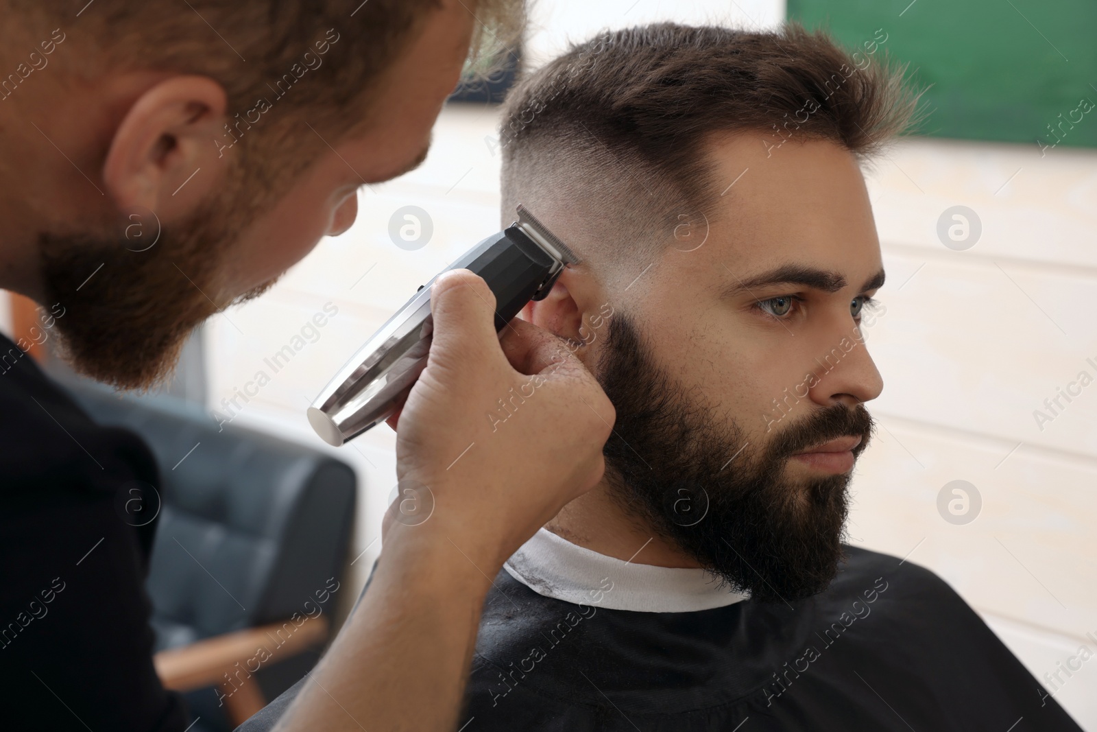 Photo of Professional hairdresser working with client in barbershop, closeup