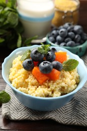 Photo of Tasty millet porridge with blueberries, pumpkin and mint in bowl on wooden table, closeup