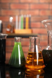 Photo of Laboratory glassware with different types of oil on mirror table indoors, closeup