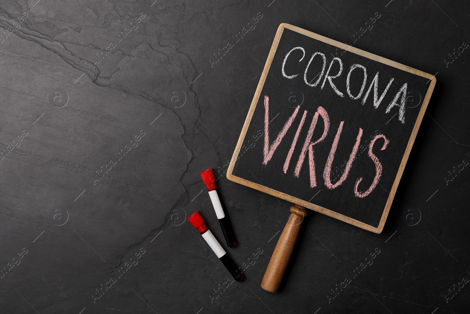 Photo of Chalkboard with phrase CORONA VIRUS and test tubes on black background, flat lay. Space for text