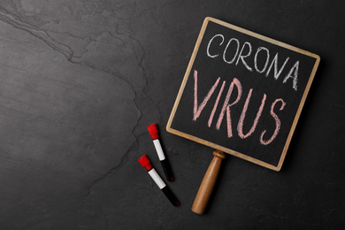 Photo of Chalkboard with phrase CORONA VIRUS and test tubes on black background, flat lay. Space for text