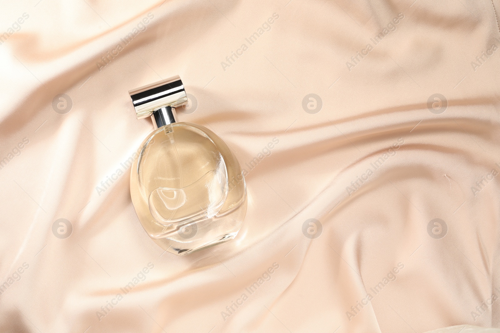 Photo of Luxury perfume in bottle on beige silk fabric, top view