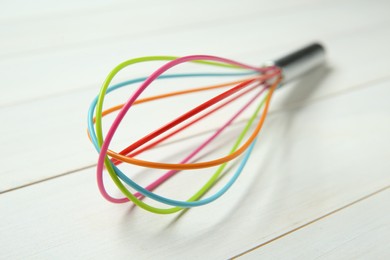 Photo of One whisk on white wooden table, closeup