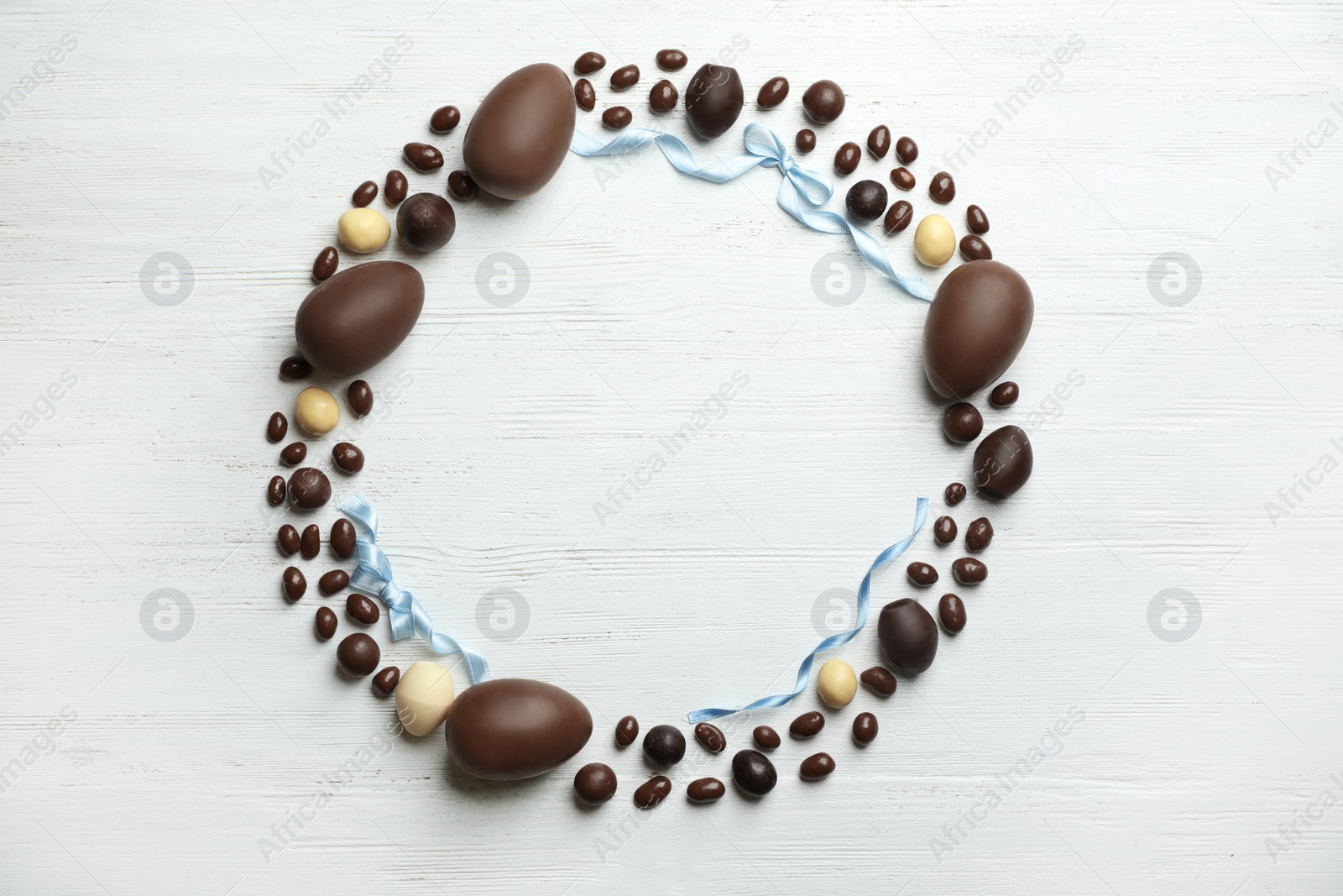 Photo of Frame made of chocolate Easter eggs on wooden background, top view with space for text