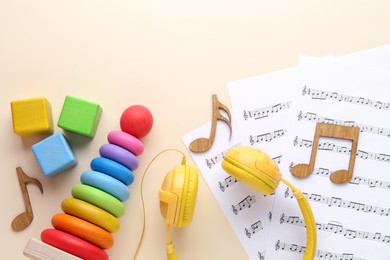 Photo of Wooden notes, music sheets, headphones and toys on beige background, flat lay with space for text. Baby song concept