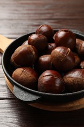 Roasted edible sweet chestnuts in baking dish on wooden table, closeup
