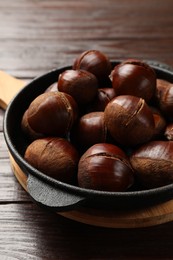 Photo of Roasted edible sweet chestnuts in baking dish on wooden table, closeup