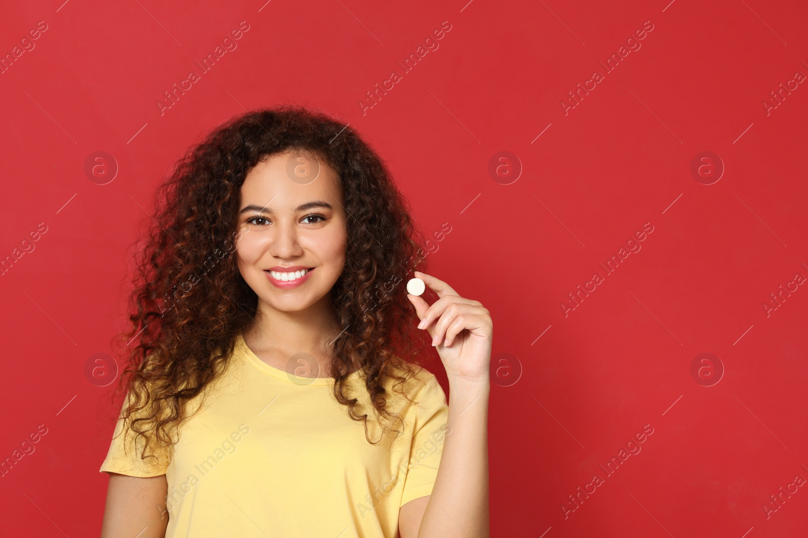Photo of African-American woman with vitamin pill on red background. Space for text