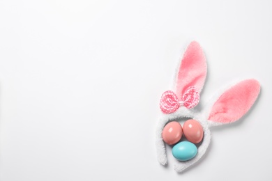 Photo of Funny headband with Easter bunny ears and dyed eggs white background, top view