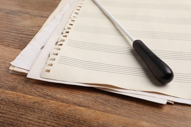 Conductor's baton and sheet music on wooden table, closeup