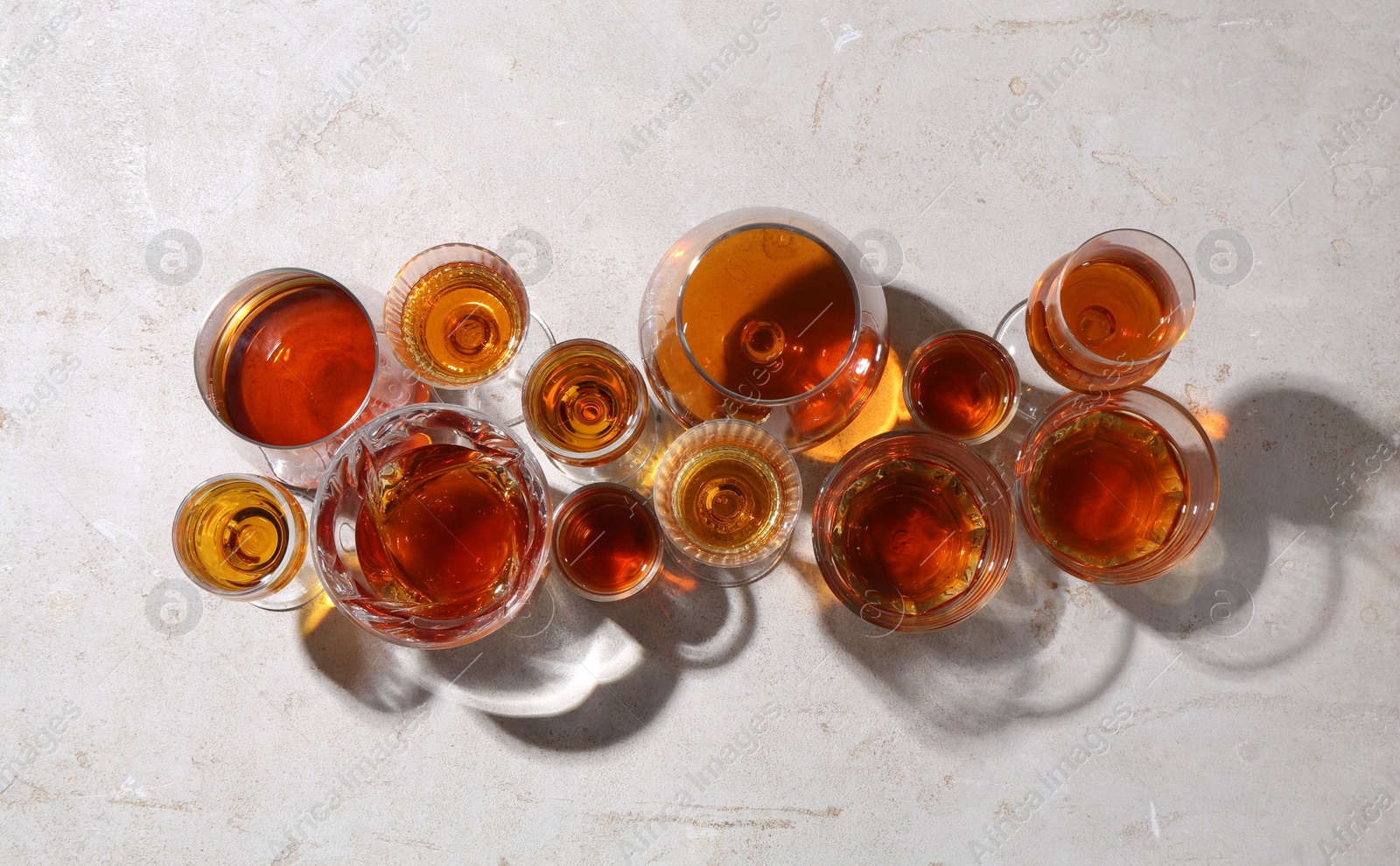 Photo of Different delicious liqueurs in glasses on light grey table, flat lay