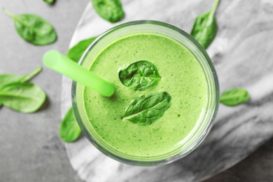 Photo of Glass of fresh green healthy spinach smoothie on grey table, top view