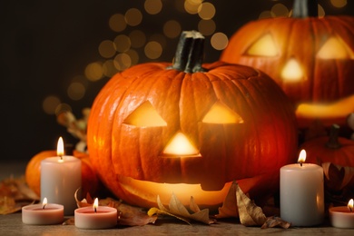 Photo of Pumpkin jack o'lanterns, autumn leaves and candles on table against blurred background. Halloween decor