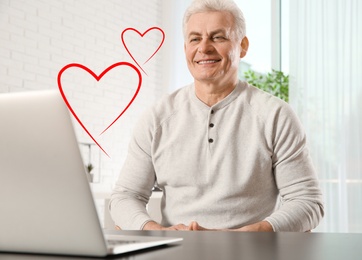 Image of Mature man visiting dating site via laptop indoors