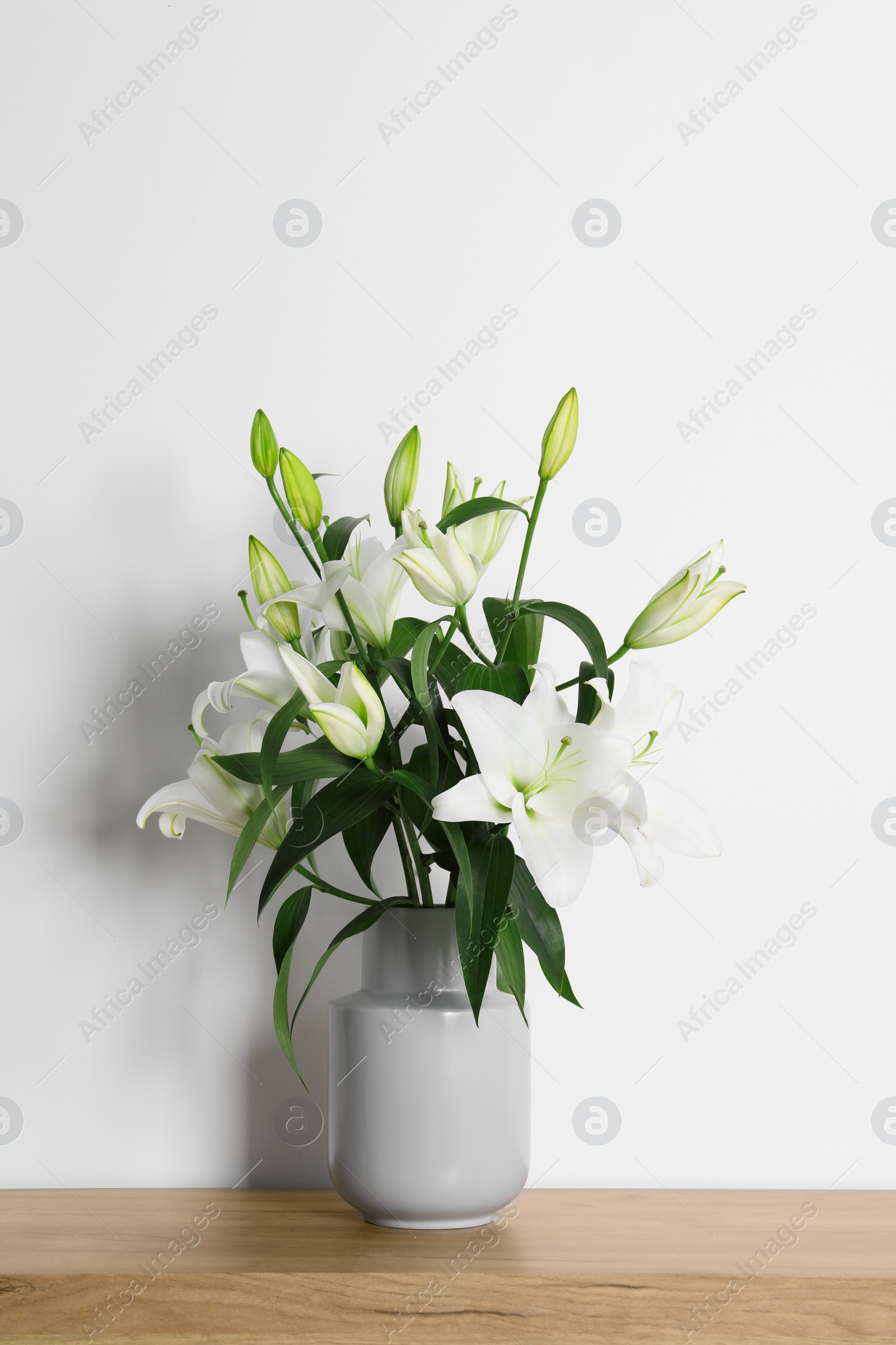 Photo of Beautiful bouquet of lily flowers in vase on wooden table near white wall