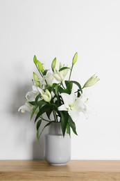 Beautiful bouquet of lily flowers in vase on wooden table near white wall