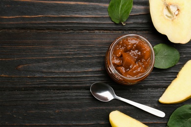 Photo of Delicious quince jam, fruits, leaves and spoon on black wooden table, flat lay