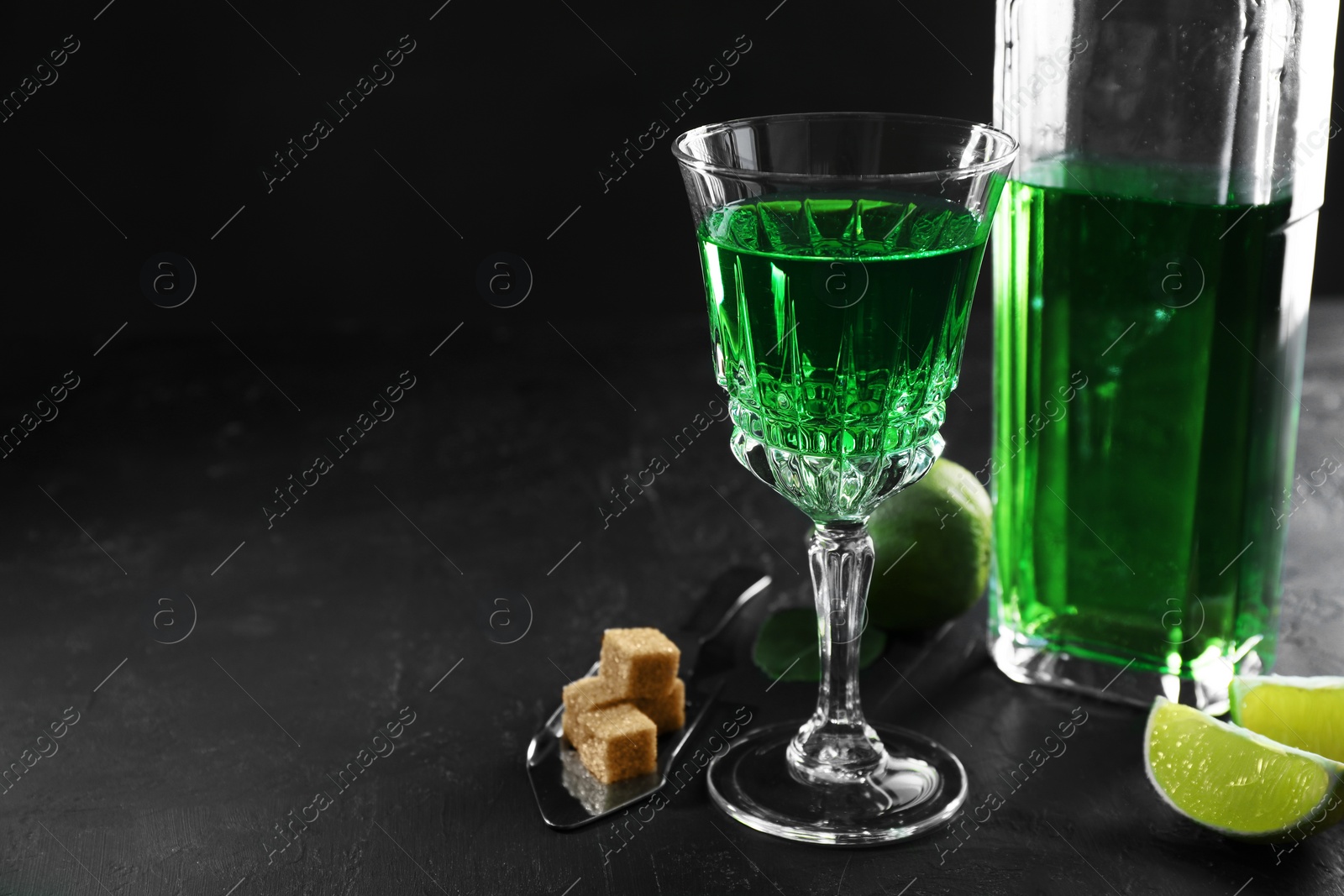 Photo of Absinthe, spoon, brown sugar and lime on black table, space for text. Alcoholic drink