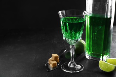 Photo of Absinthe, spoon, brown sugar and lime on black table, space for text. Alcoholic drink