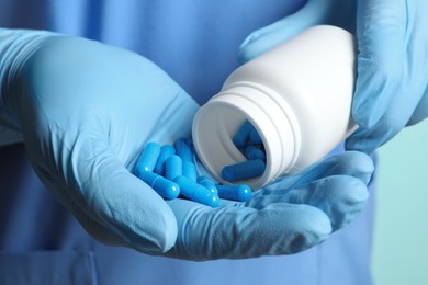 Photo of Doctor pouring pills from bottle onto hand on turquoise background, closeup