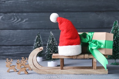 Photo of Sleigh with gift box and Santa hat on wooden table