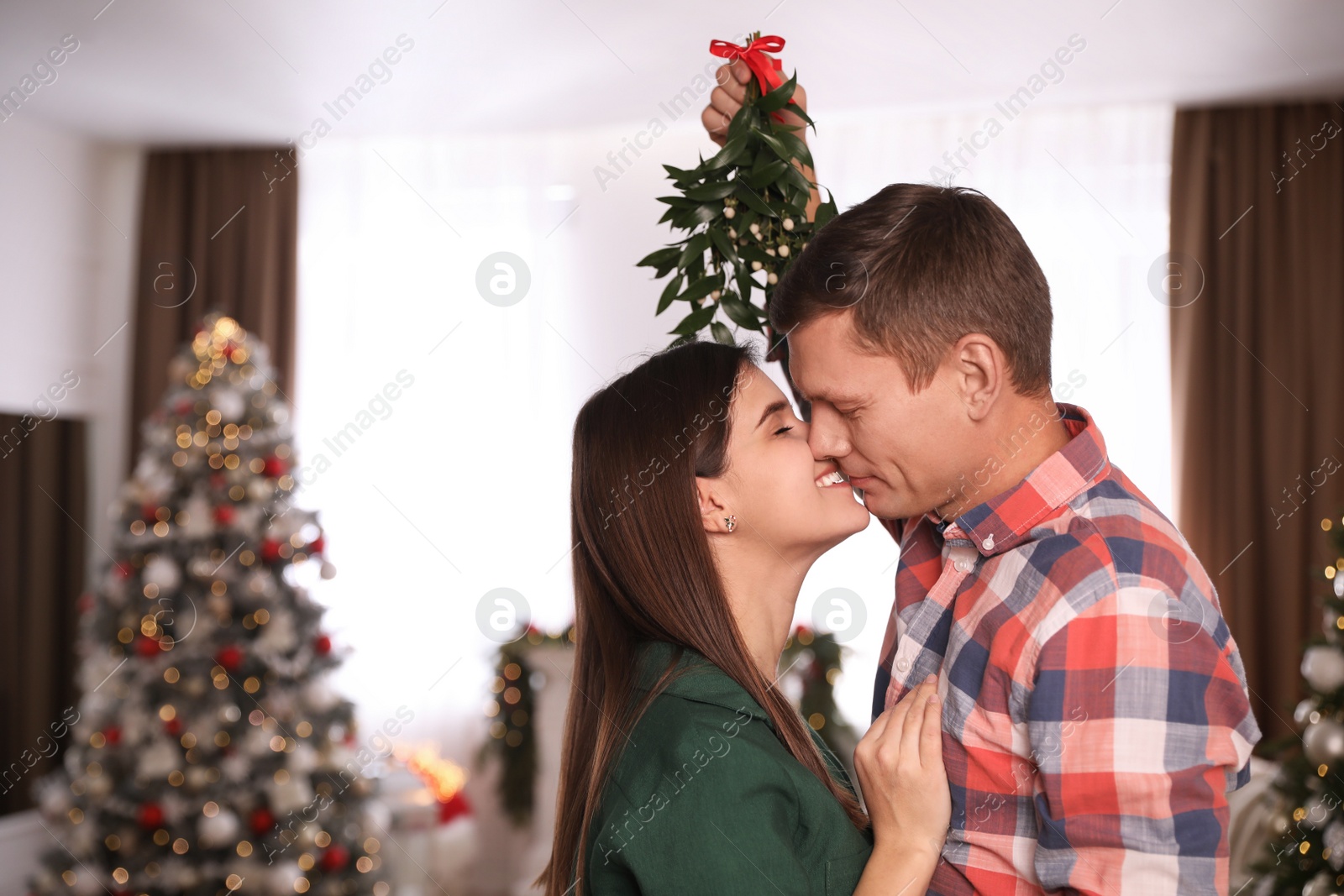 Photo of Couple kissing under mistletoe in room decorated for Christmas