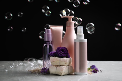 Photo of Set of hair cosmetic products, flowers and soap bubbles on black background