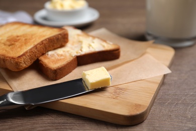Photo of Board with fresh toasts and butter on wooden table, closeup