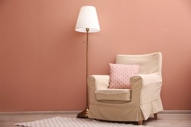 Photo of Comfortable armchair and lamp near pink wall indoors. Space for text