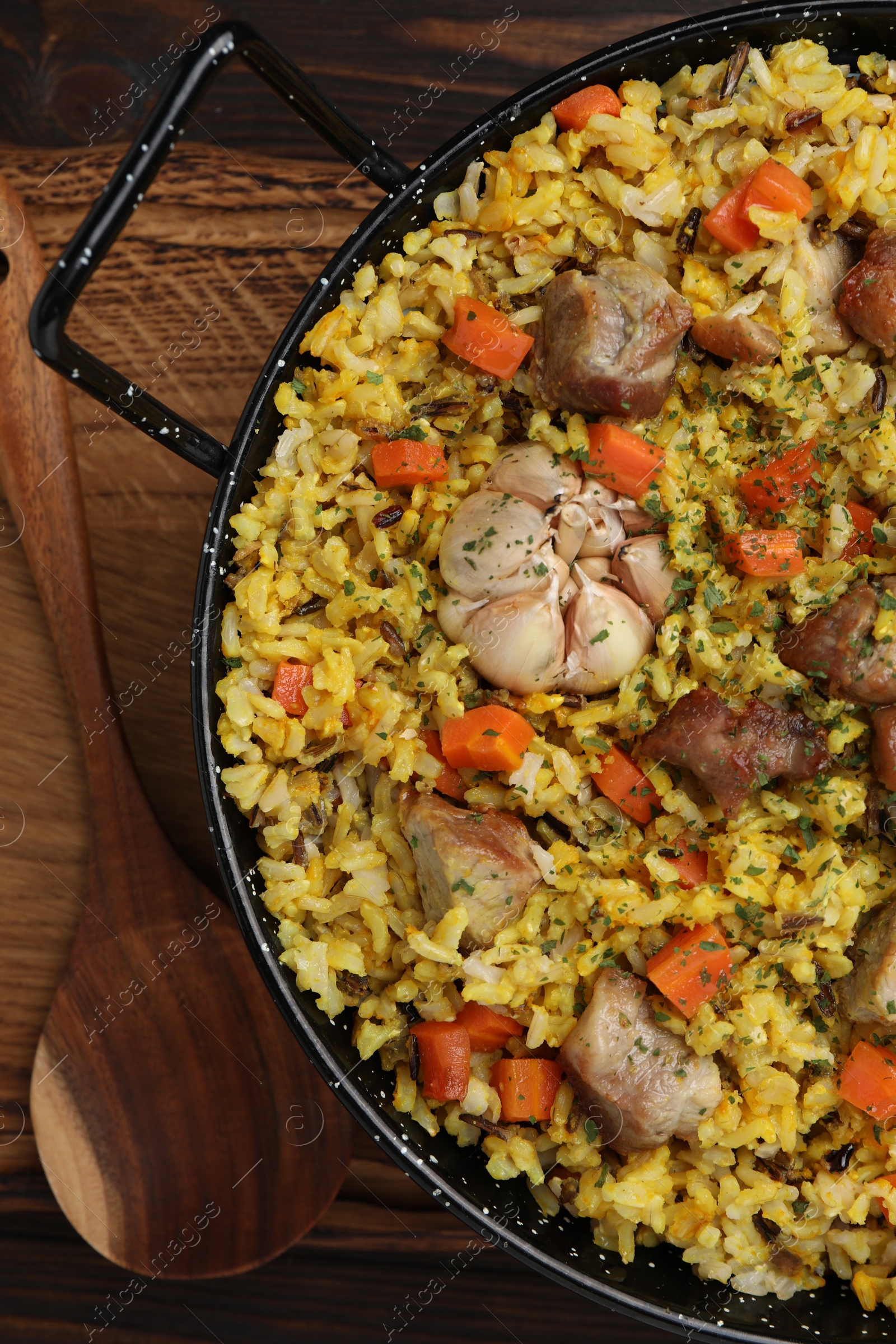 Photo of Delicious pilaf with meat, carrot and garlic served on wooden table, flat lay