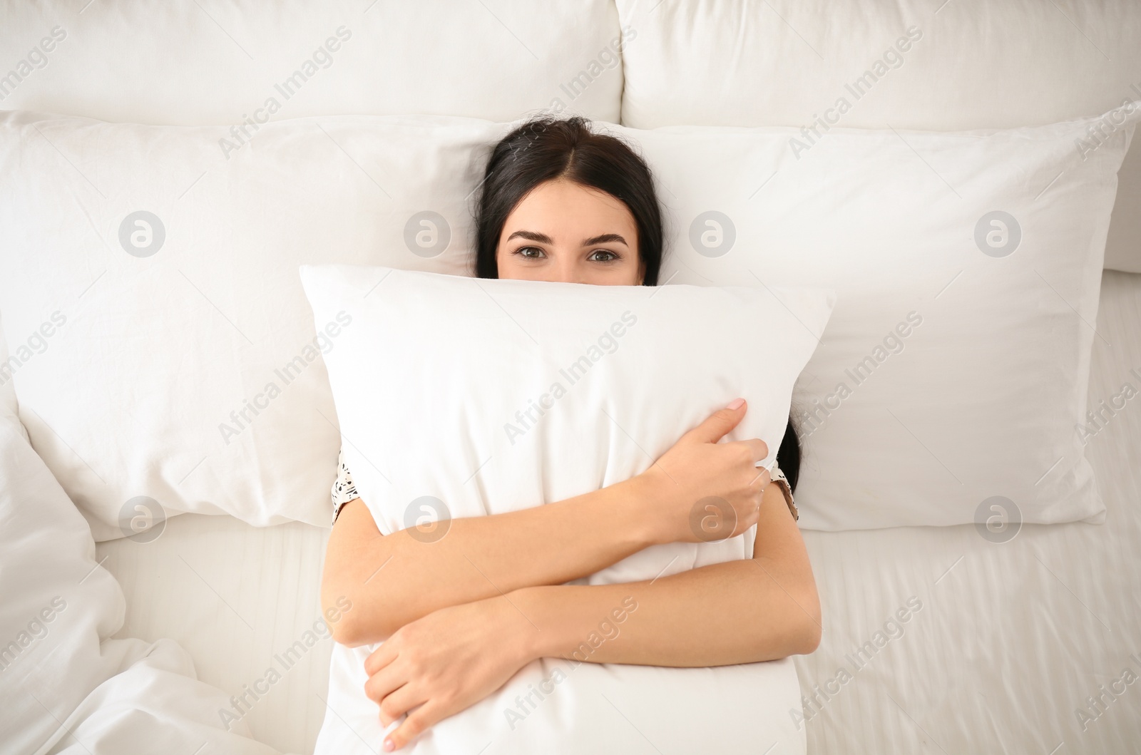 Photo of Young woman with pillow in bed, top view. Lazy morning