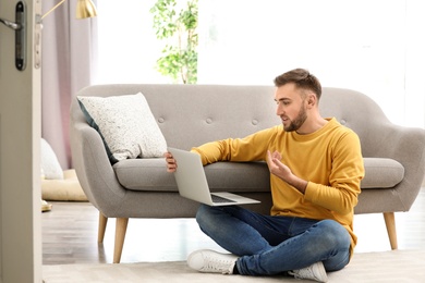 Photo of Young man using video chat on laptop in living room