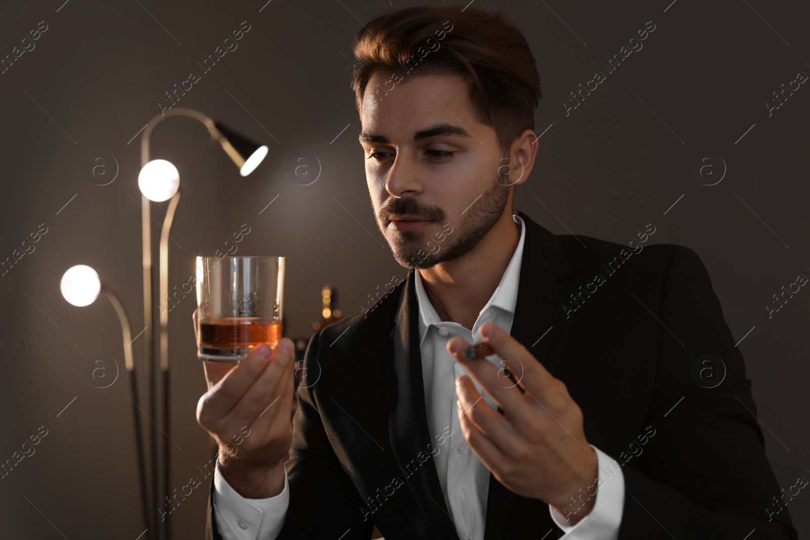 Photo of Young man with glass of whiskey and cigar at home