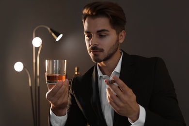 Young man with glass of whiskey and cigar at home