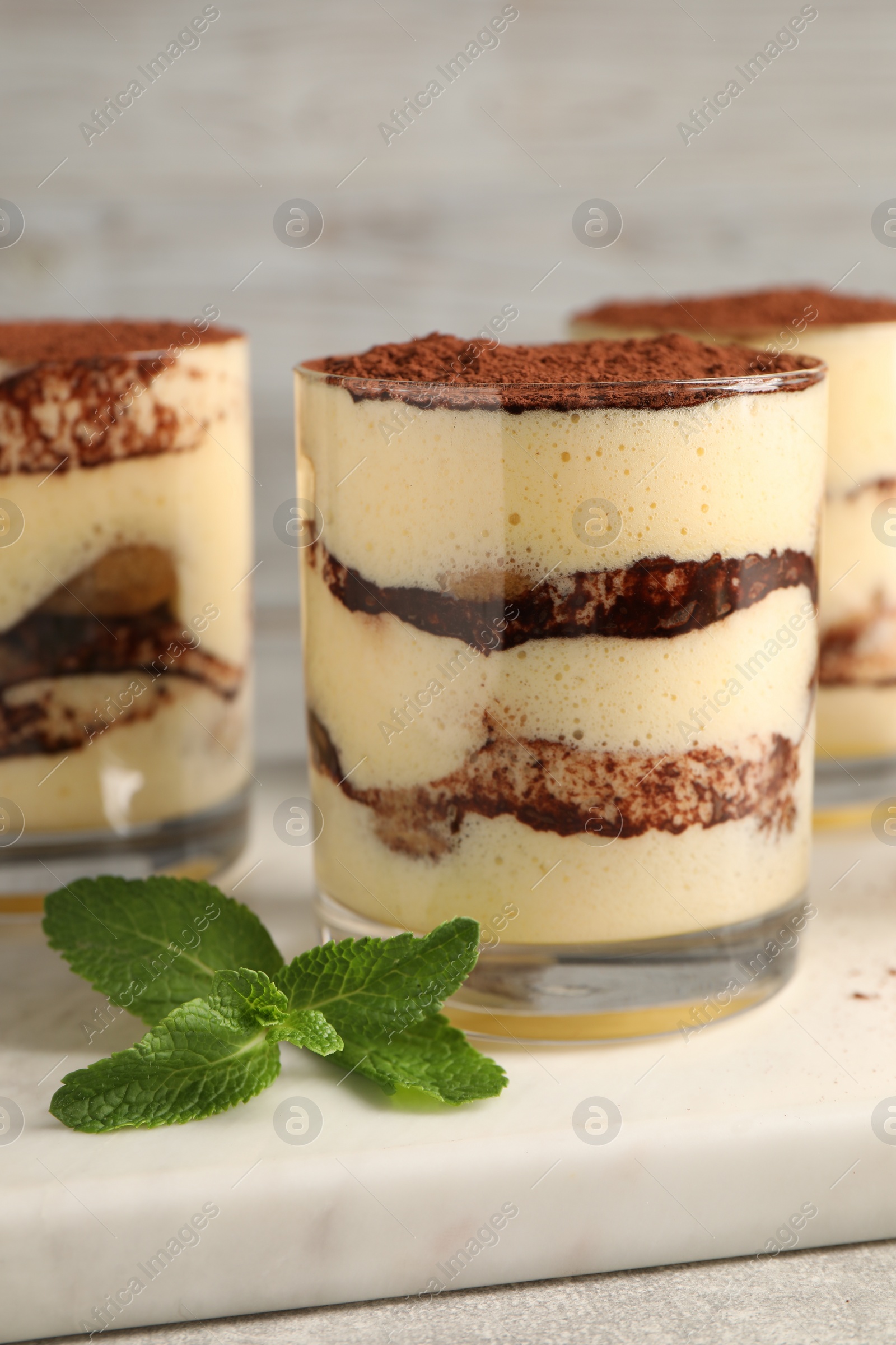 Photo of Delicious tiramisu in glasses and mint on table, closeup