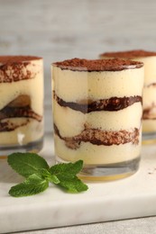 Delicious tiramisu in glasses and mint on table, closeup