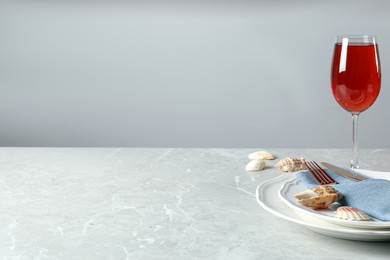 Elegant setting with glass of red wine and seashells on grey marble table. Space for text