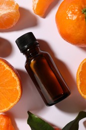 Aromatic tangerine essential oil in bottle surrounded by citrus fruits on white table, flat lay