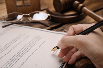 Woman signing last will and testament at wooden table, closeup
