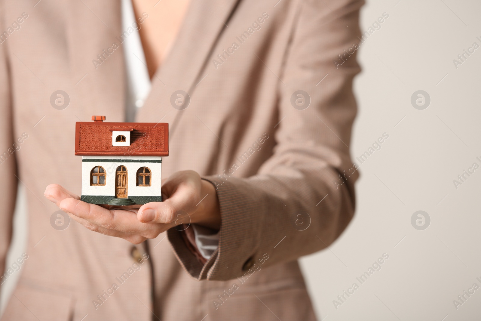 Photo of Female agent holding house model on light background, closeup. Home insurance