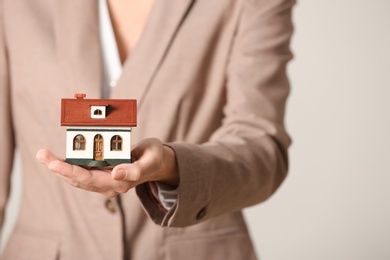 Female agent holding house model on light background, closeup. Home insurance