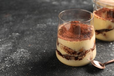 Photo of Delicious tiramisu in glasses and spoon on grey textured table, closeup. Space for text