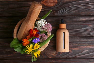 Photo of Glass bottle of aromatic essential oil and mortar with different herbs on wooden table, flat lay. Space for text