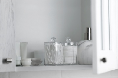 Photo of Cotton buds and pads in transparent holders near toiletries on shelf