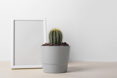 Photo of Beautiful cactus in pot and frame on beige table