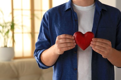 Closeup of man holding red heart indoors, space for text. Volunteer concept