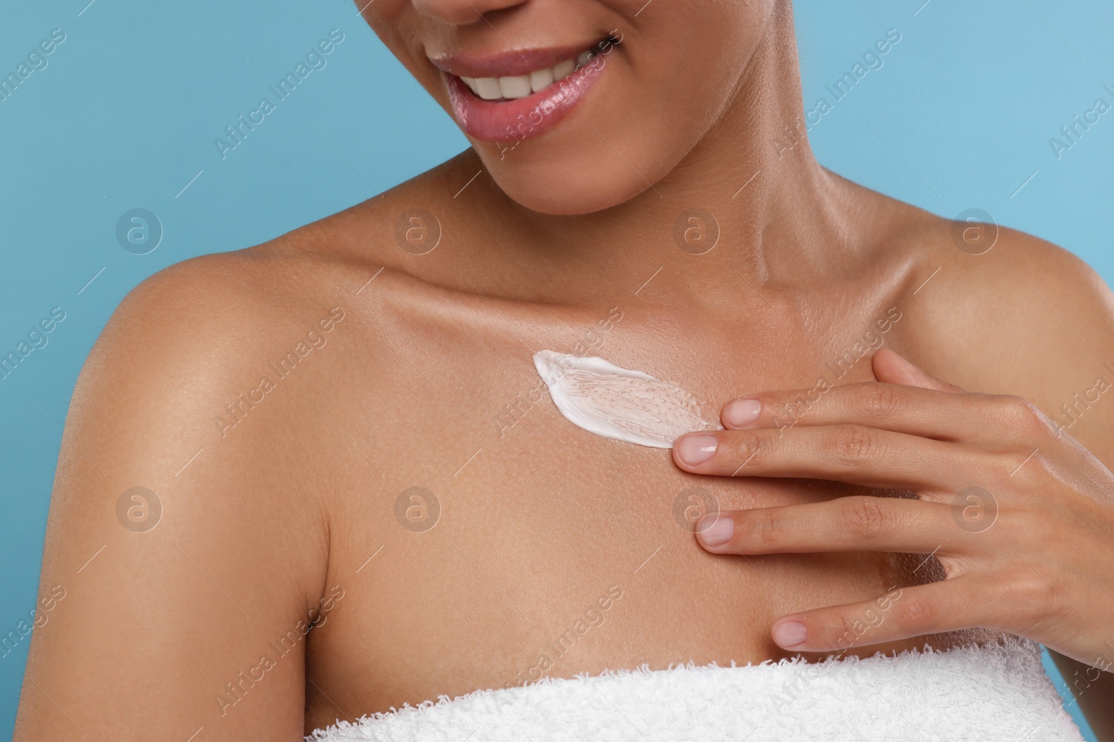 Photo of Young woman applying cream onto body on light blue background, closeup